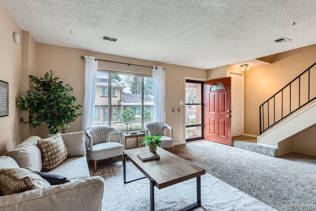 living area featuring visible vents, stairway, carpet, and a textured ceiling
