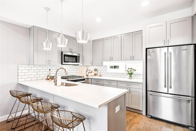 kitchen featuring stainless steel appliances, light countertops, a sink, a peninsula, and a kitchen breakfast bar