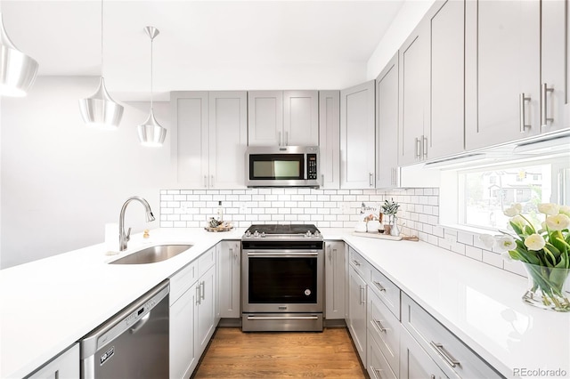 kitchen with decorative light fixtures, stainless steel appliances, light countertops, decorative backsplash, and a sink