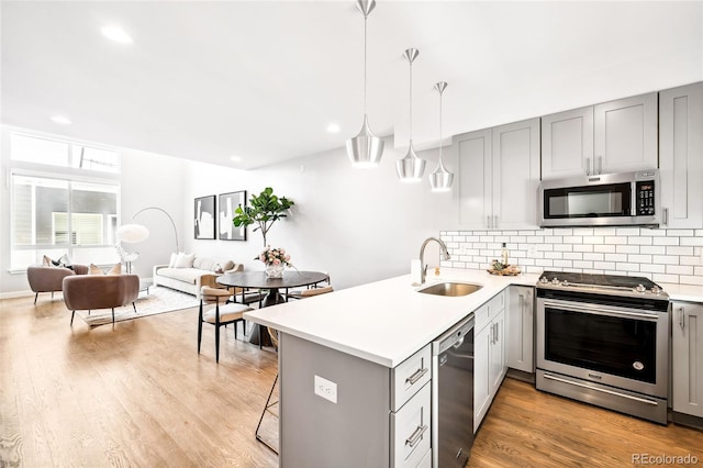 kitchen featuring stainless steel appliances, a peninsula, a sink, light countertops, and pendant lighting