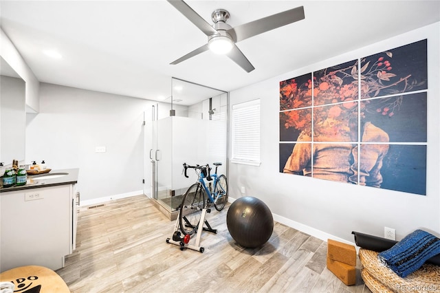 exercise room featuring ceiling fan, light wood-style flooring, and baseboards