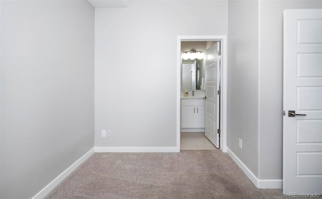 unfurnished bedroom featuring light colored carpet, a sink, baseboards, and ensuite bathroom