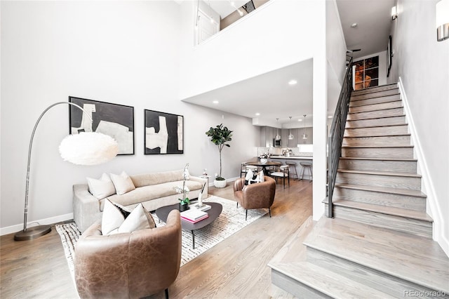 living room with a towering ceiling, light wood finished floors, stairs, and baseboards