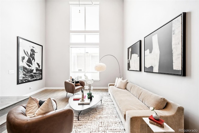 living area with a high ceiling, light wood-type flooring, and baseboards