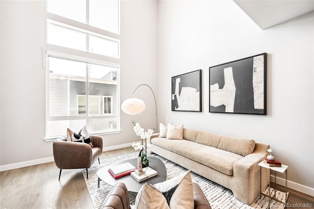 living area featuring a towering ceiling, baseboards, and wood finished floors