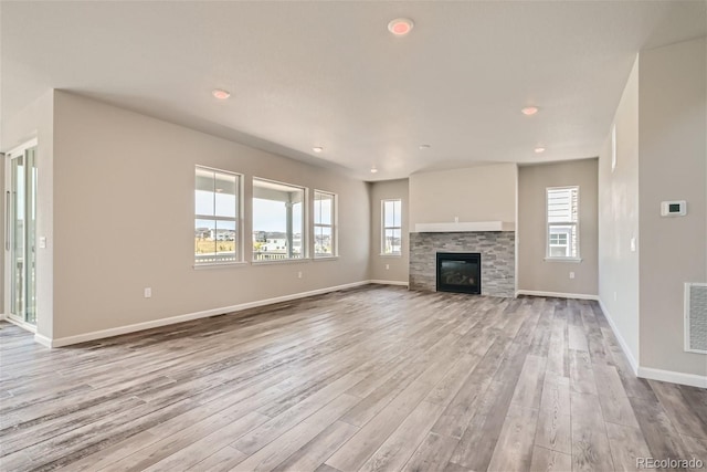 unfurnished living room with a stone fireplace, a wealth of natural light, and light wood-type flooring