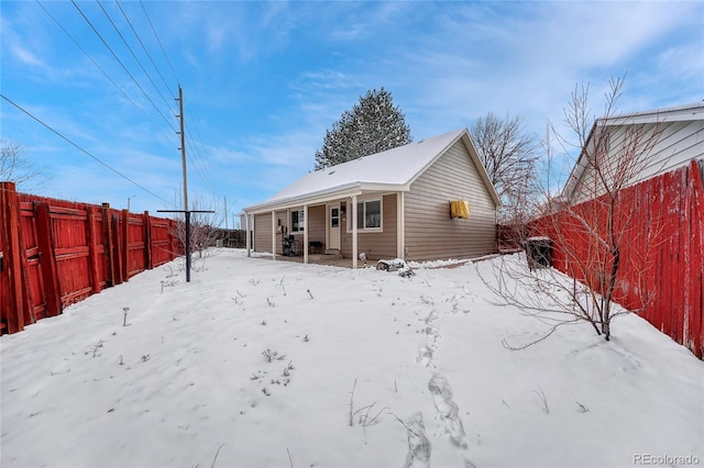 snow covered back of property with a porch and fence