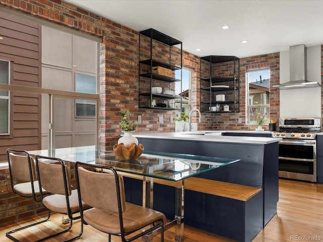 8336 E 35th Ave, Denver, CO 80238 - kitchen with range with two ovens, wall chimney range hood, open shelves, a sink, and brick wall