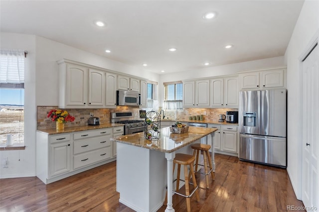 kitchen featuring light stone counters, stainless steel appliances, white cabinets, and a center island