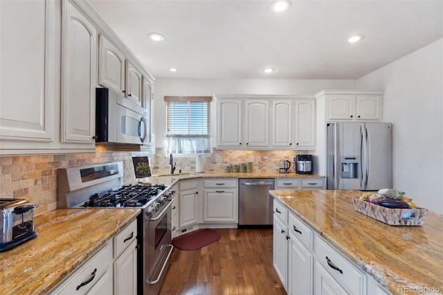 kitchen featuring appliances with stainless steel finishes, light stone countertops, dark wood-type flooring, white cabinetry, and tasteful backsplash