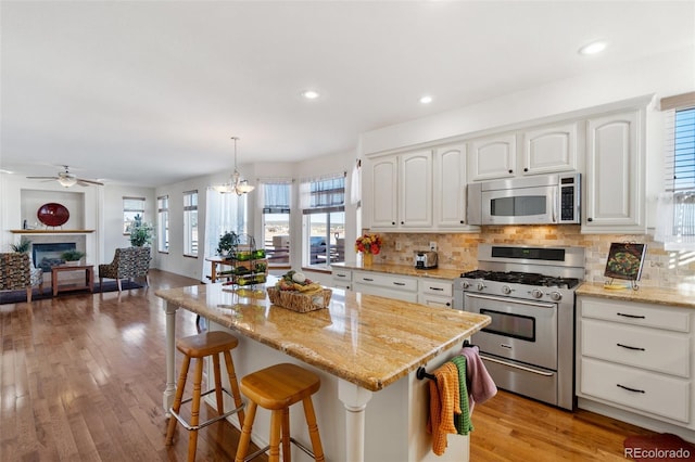 kitchen with appliances with stainless steel finishes, a center island, white cabinets, decorative light fixtures, and tasteful backsplash