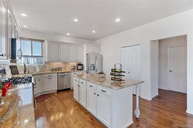 kitchen featuring stainless steel appliances, white cabinets, a center island, backsplash, and light stone countertops