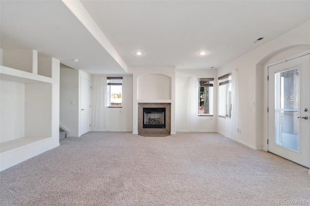 unfurnished living room with a tiled fireplace and light carpet