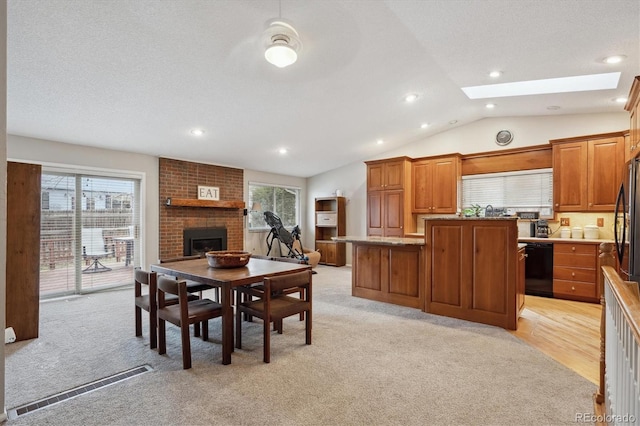 dining area featuring a fireplace, vaulted ceiling with skylight, light colored carpet, and a textured ceiling