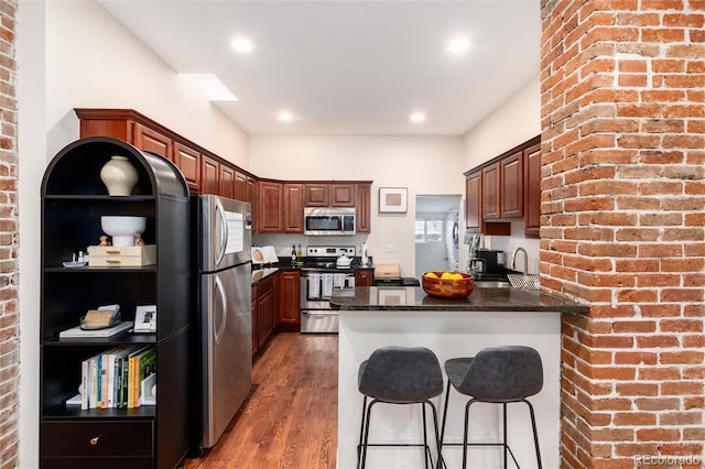 kitchen featuring a peninsula, wood finished floors, a breakfast bar, stainless steel appliances, and brick wall