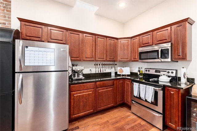 kitchen with dark stone counters, light wood-type flooring, wine cooler, appliances with stainless steel finishes, and recessed lighting