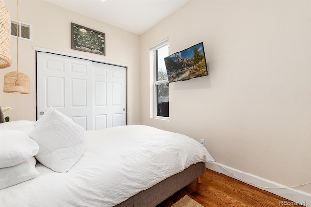 bedroom with baseboards, a closet, visible vents, and wood finished floors