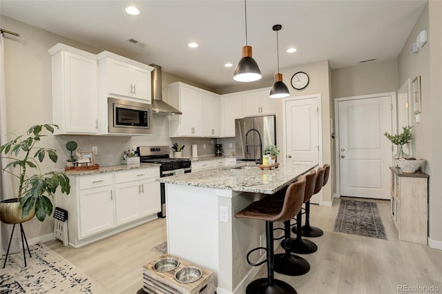 9279 Merino Ct Unit D, Littleton, CO 80125 - kitchen with appliances with stainless steel finishes, wall chimney exhaust hood, a sink, light wood-style flooring, and white cabinets