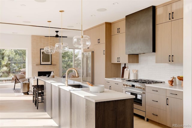 kitchen with pendant lighting, wall chimney range hood, sink, premium appliances, and an island with sink