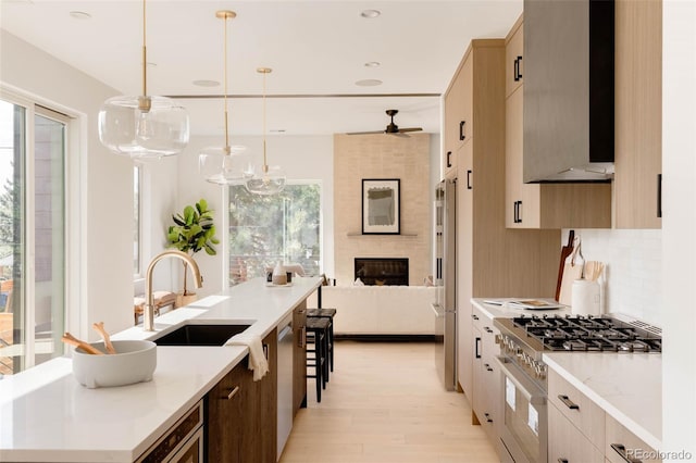 kitchen with pendant lighting, sink, wall chimney range hood, high end appliances, and tasteful backsplash