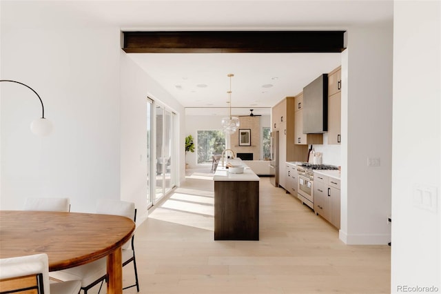 16133 W 14th Ave, Golden, CO 80401 - kitchen with light hardwood / wood-style flooring, a kitchen island with sink, hanging light fixtures, stainless steel range, and beamed ceiling