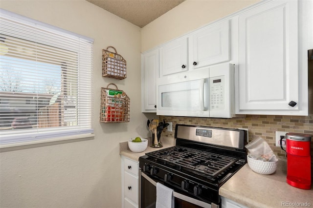 kitchen with stainless steel gas range oven, decorative backsplash, white microwave, and white cabinets