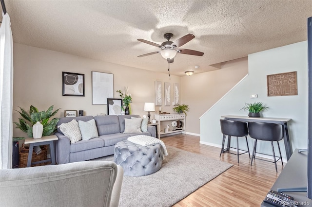 living room featuring a ceiling fan, wood finished floors, baseboards, and a textured ceiling