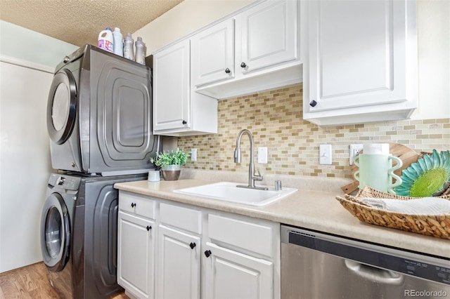 laundry room featuring a sink, a textured ceiling, stacked washing maching and dryer, light wood-style floors, and laundry area