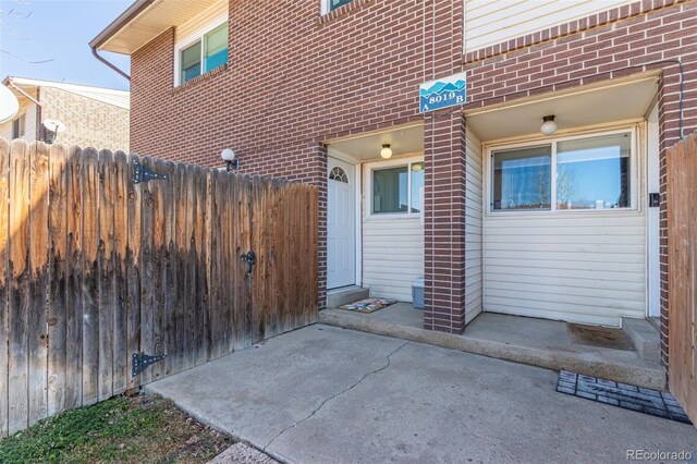 doorway to property featuring brick siding and fence