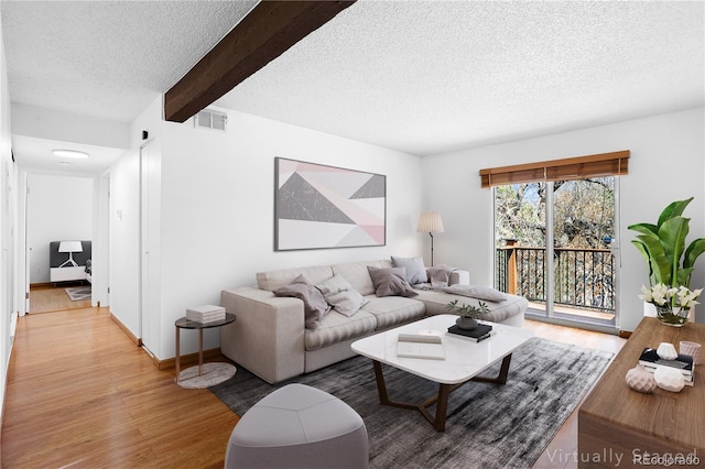 living area with a textured ceiling, light wood finished floors, beam ceiling, and baseboards