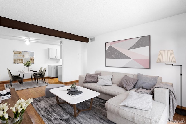 living room featuring beamed ceiling, light wood finished floors, baseboards, and a ceiling fan
