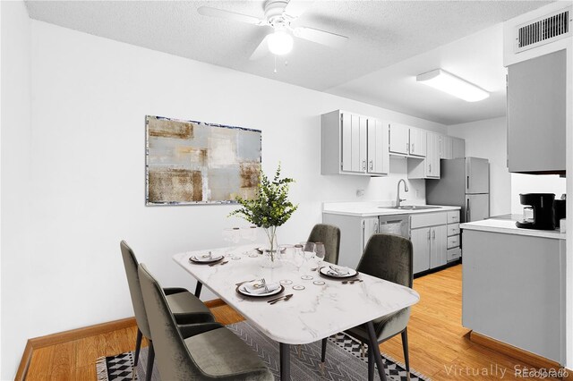 dining area featuring light wood-style flooring, a ceiling fan, a textured ceiling, and baseboards