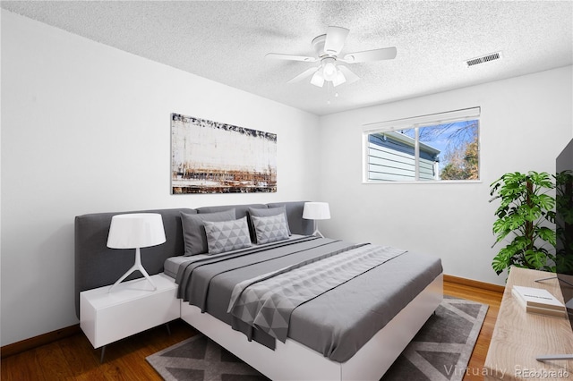 bedroom with wood finished floors, baseboards, a textured ceiling, and a ceiling fan