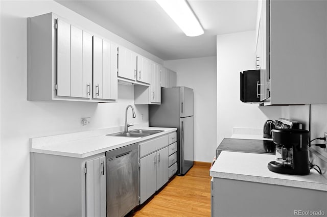 kitchen featuring stainless steel appliances, a sink, light wood finished floors, and light countertops