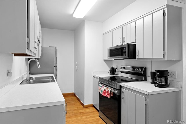 kitchen featuring appliances with stainless steel finishes, a sink, light wood finished floors, light countertops, and baseboards