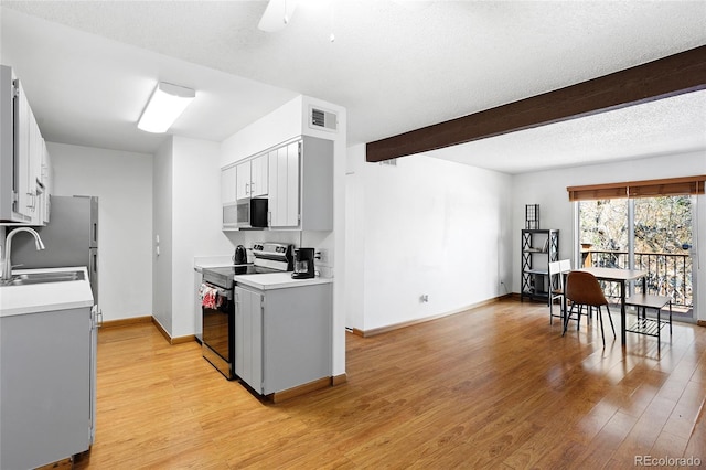 kitchen with stainless steel appliances, a sink, light countertops, light wood-type flooring, and beam ceiling