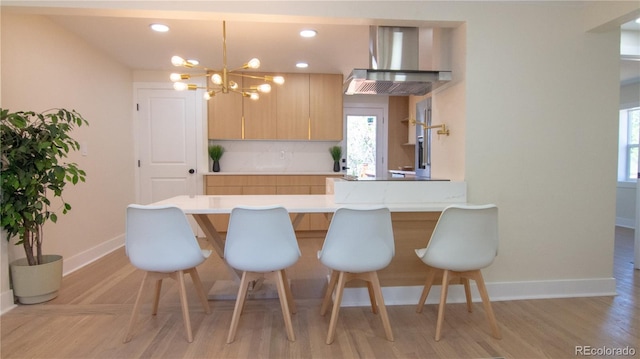 2441 W 55th Ave, Denver, CO 80221 - kitchen featuring wall chimney exhaust hood, baseboards, a breakfast bar area, a chandelier, and a peninsula