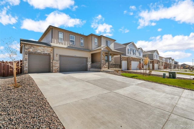 townhome / multi-family property featuring stone siding, fence, a residential view, concrete driveway, and an attached garage