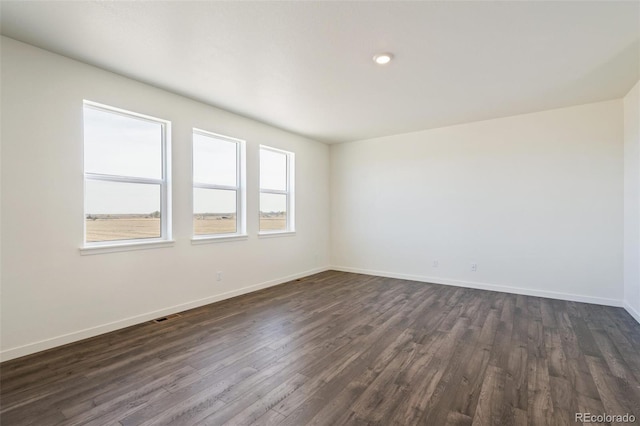 unfurnished room featuring visible vents, dark wood-type flooring, and baseboards