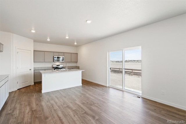 kitchen with dark wood-style floors, baseboards, an island with sink, gray cabinets, and stainless steel appliances