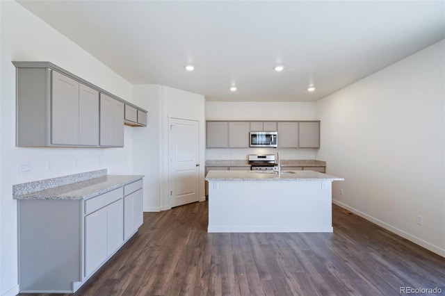 kitchen featuring stainless steel microwave, gray cabinetry, dark wood finished floors, a center island with sink, and gas stove