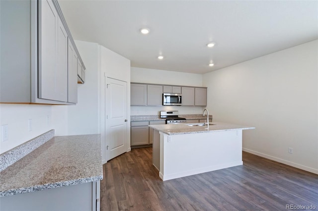 kitchen with a center island with sink, gray cabinets, a sink, stainless steel appliances, and dark wood-style flooring