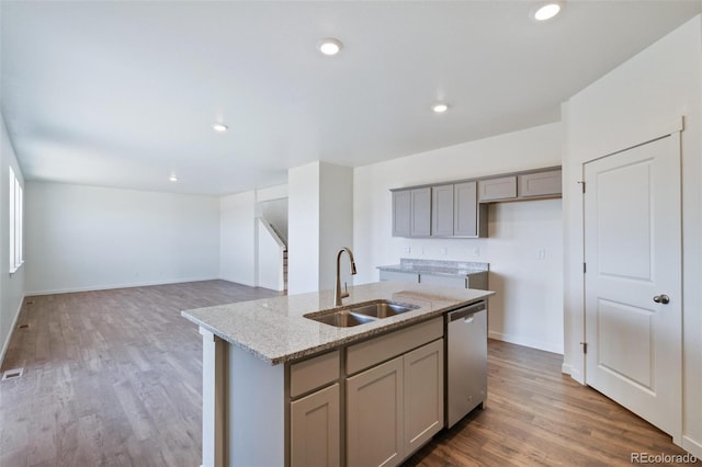 kitchen featuring an island with sink, gray cabinets, stainless steel dishwasher, wood finished floors, and a sink