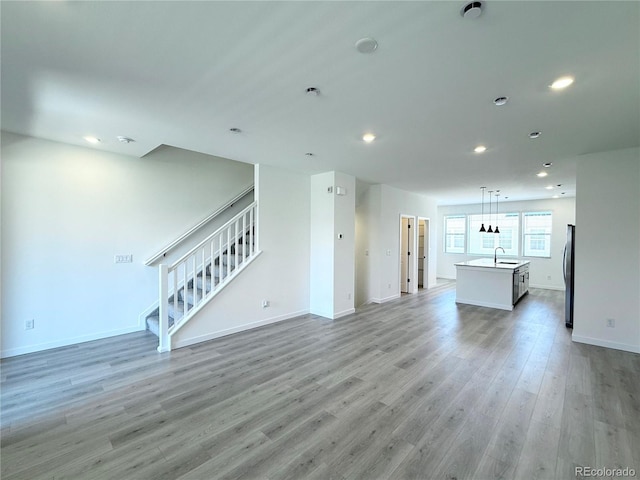 9662 Browns Peak Cir, Littleton, CO 80125 - unfurnished living room with stairs, light wood-style floors, recessed lighting, baseboards, and a sink