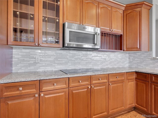 2485 Greensborough Cir, Highlands Ranch, CO 80129 - kitchen featuring stainless steel microwave, light stone counters, black electric stovetop, and glass insert cabinets