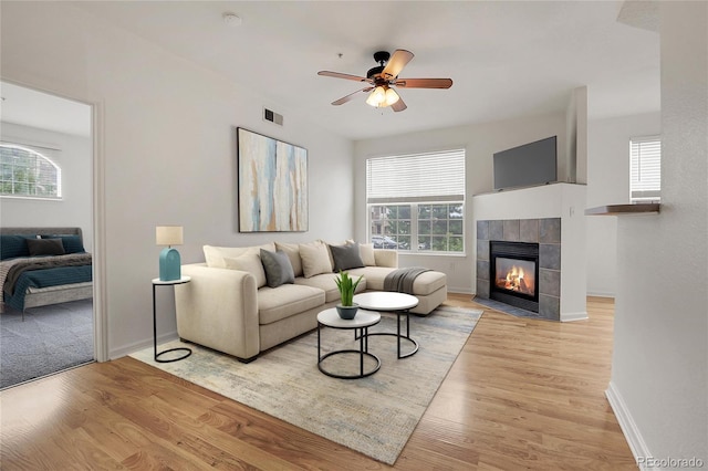 living room featuring plenty of natural light, a tiled fireplace, and light wood-type flooring