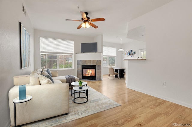 living room featuring light hardwood / wood-style floors, a tile fireplace, ceiling fan, and a healthy amount of sunlight