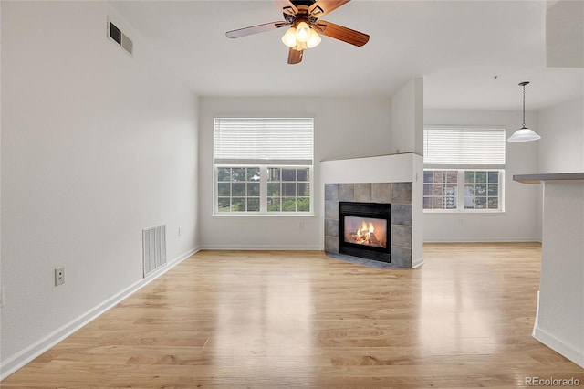 unfurnished living room featuring ceiling fan, a tiled fireplace, and light wood-type flooring