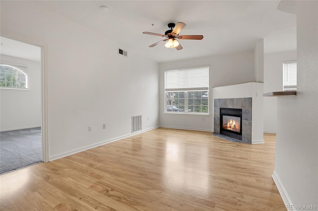 unfurnished living room featuring ceiling fan, a wealth of natural light, light hardwood / wood-style flooring, and a fireplace