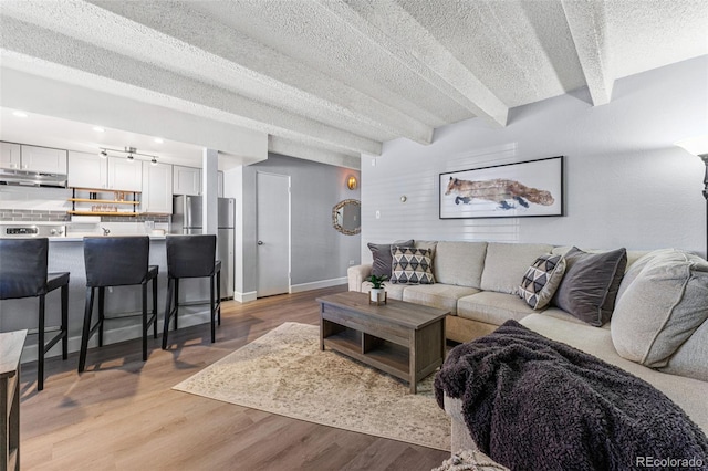 living room featuring light wood-type flooring, a textured ceiling, and beamed ceiling